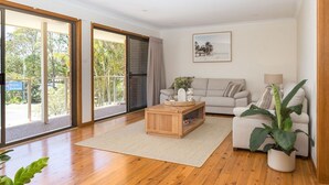 A spacious living room with a wooden coffee table, a beige sofa, and a large potted plant. - Byron's Beach House Mylestom
Entire home in Mylestom, Australia (Mylestom)