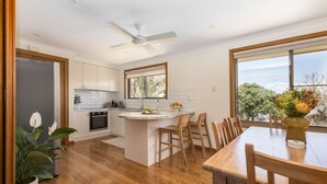 A modern kitchen with white cabinets, a wooden dining table, and a large window. - Byron's Beach House Mylestom
Entire home in Mylestom, Australia (Mylestom)