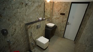 A bathroom with a marble wall, a white sink, a toilet, and a shower. - Hotel New Grand (Deoghar)