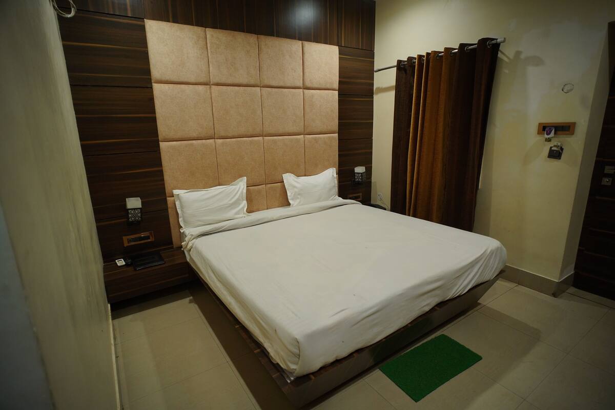 Una habitación de hotel con una cama grande, cabecera de madera y una alfombra verde.