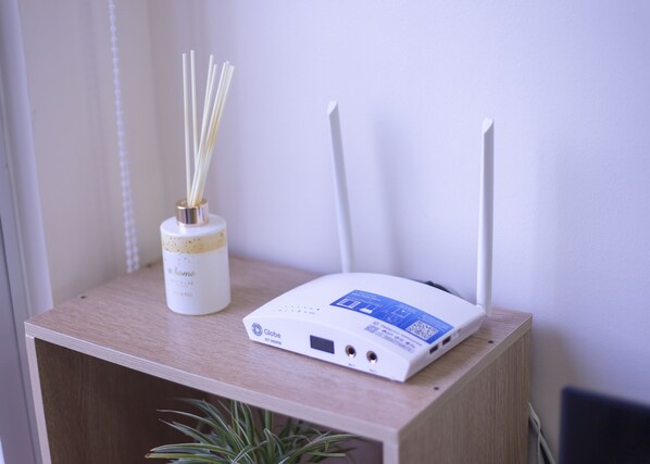 A white router on a wooden table with a white bottle labeled "home" and a plant.