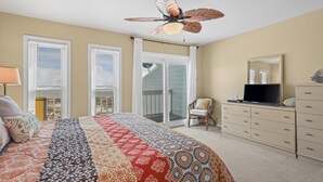 Una camera da letto con un letto grande, un ventilatore a soffitto, un comò, una TV e un'ampia porta scorrevole che dà su un balcone.