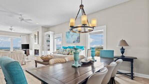Un salon spacieux doté d’une grande fenêtre, un coin repas avec une table en bois et un espace détente confortable avec un canapé et des fauteuils.