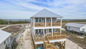 A two-story beach house with a balcony, a patio with outdoor furniture, and a view of the ocean.