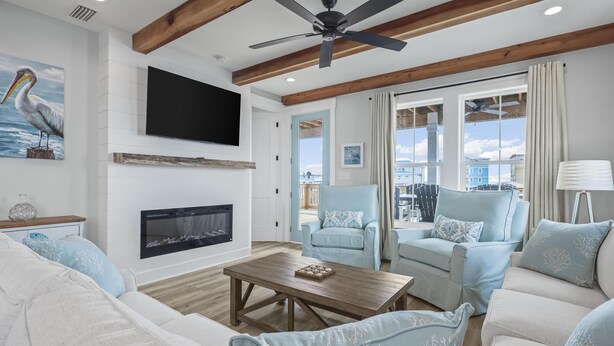 A spacious living room with a fireplace, a ceiling fan, and a large window offering a view of the outdoors.