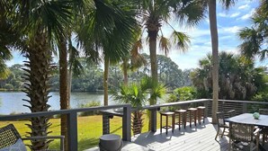 A deck with outdoor furniture, a view of a lake, and palm trees. - 116 Sea Otter - Resort Access & Golf Cart! (Fripp Island)