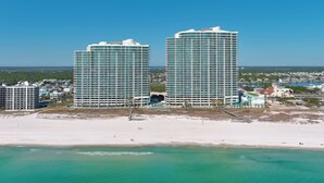 Ein Hochhaus-Hotel mit mehreren Stockwerken, ein Strand im Vordergrund und ein klarer, blauer Himmel.