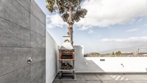 Un espacio exterior moderno con un horno de ladrillo, un árbol y vistas a colinas distantes.