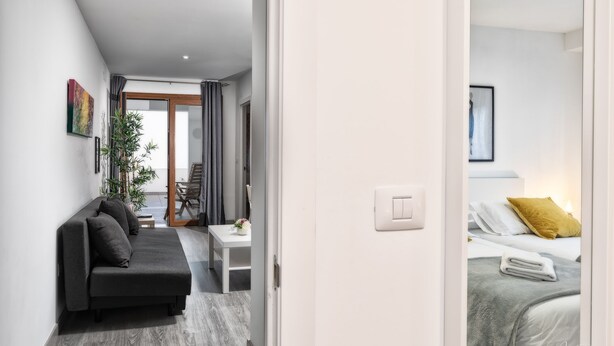 Una habitación de hotel moderna con un sofá, una mesita con un florero y una cama con un cojín amarillo.