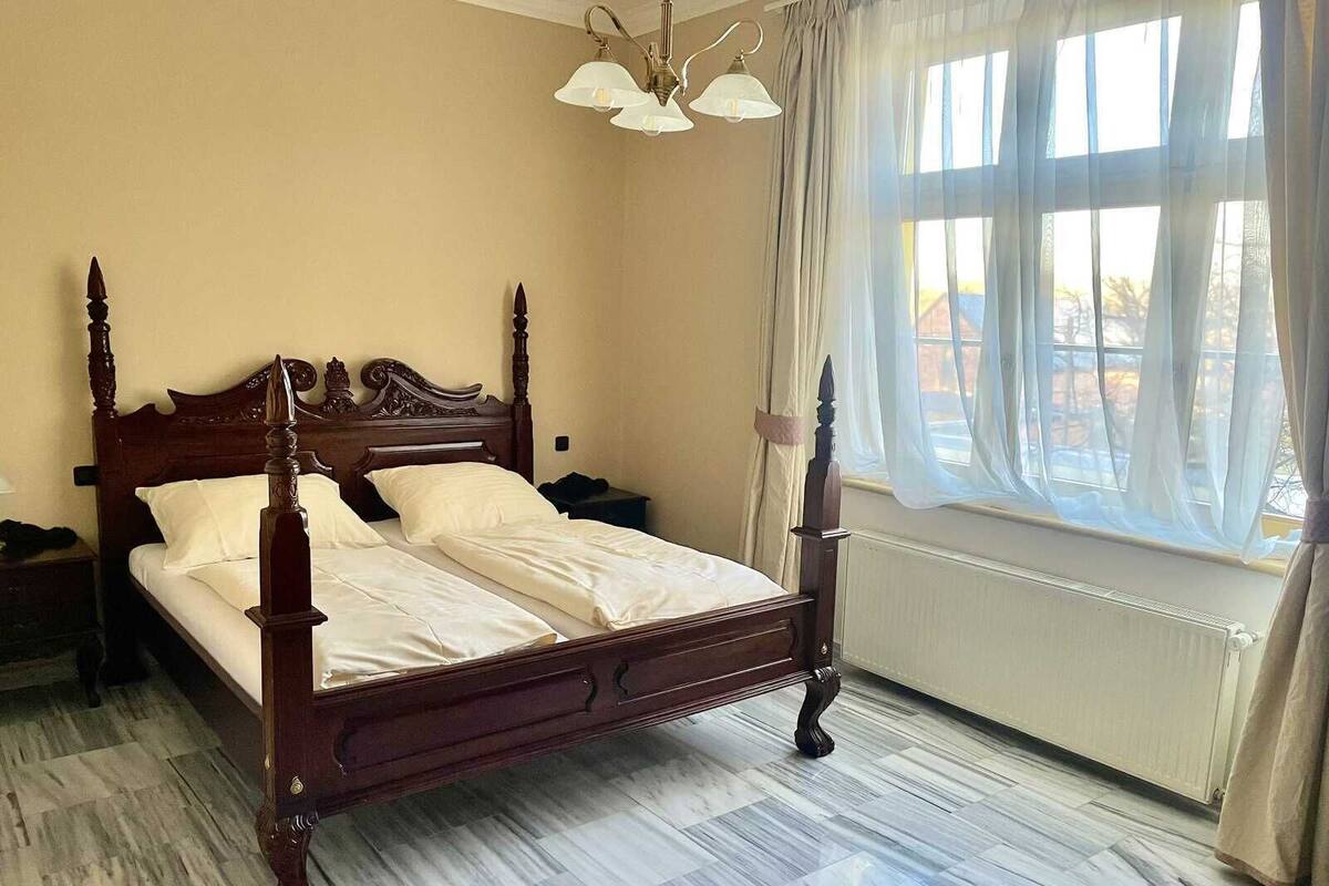 A four-poster bed with white linens, a wooden headboard, and a nightstand with a lamp.