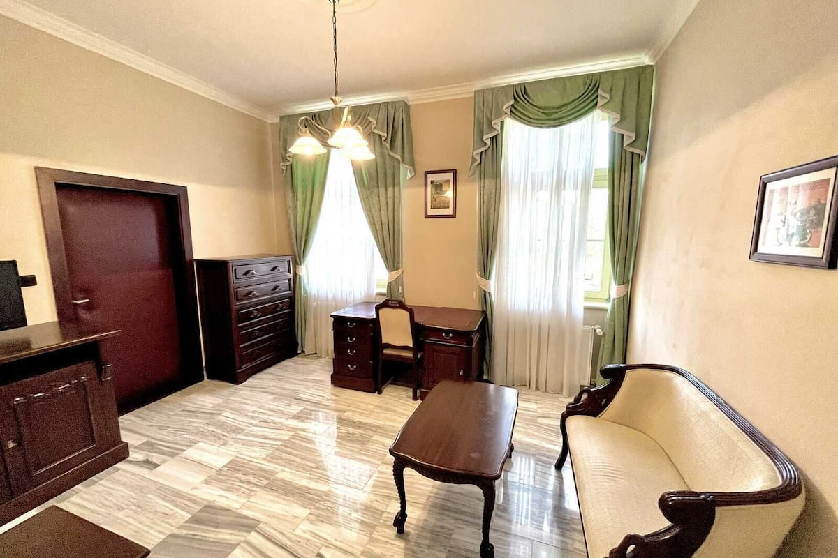 A room with a wooden desk, a sofa, a dresser, and a chandelier.