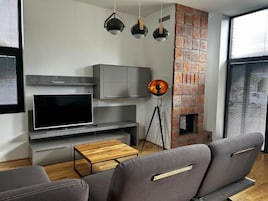 Una sala de estar moderna con una televisión de pantalla plana, sofás grises, una mesa de centro de madera y una chimenea de ladrillo.