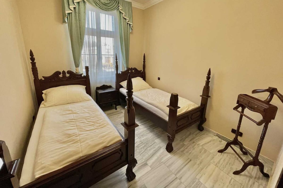 A room with two wooden beds, a nightstand, a wooden chair, and a window with curtains.