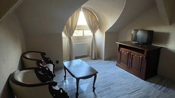 A room with a sloped ceiling, a television on a cabinet, a table, and a chair.