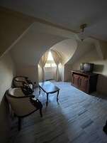 Una habitación con techo inclinado, un televisor en un mueble, una mesa y una silla.