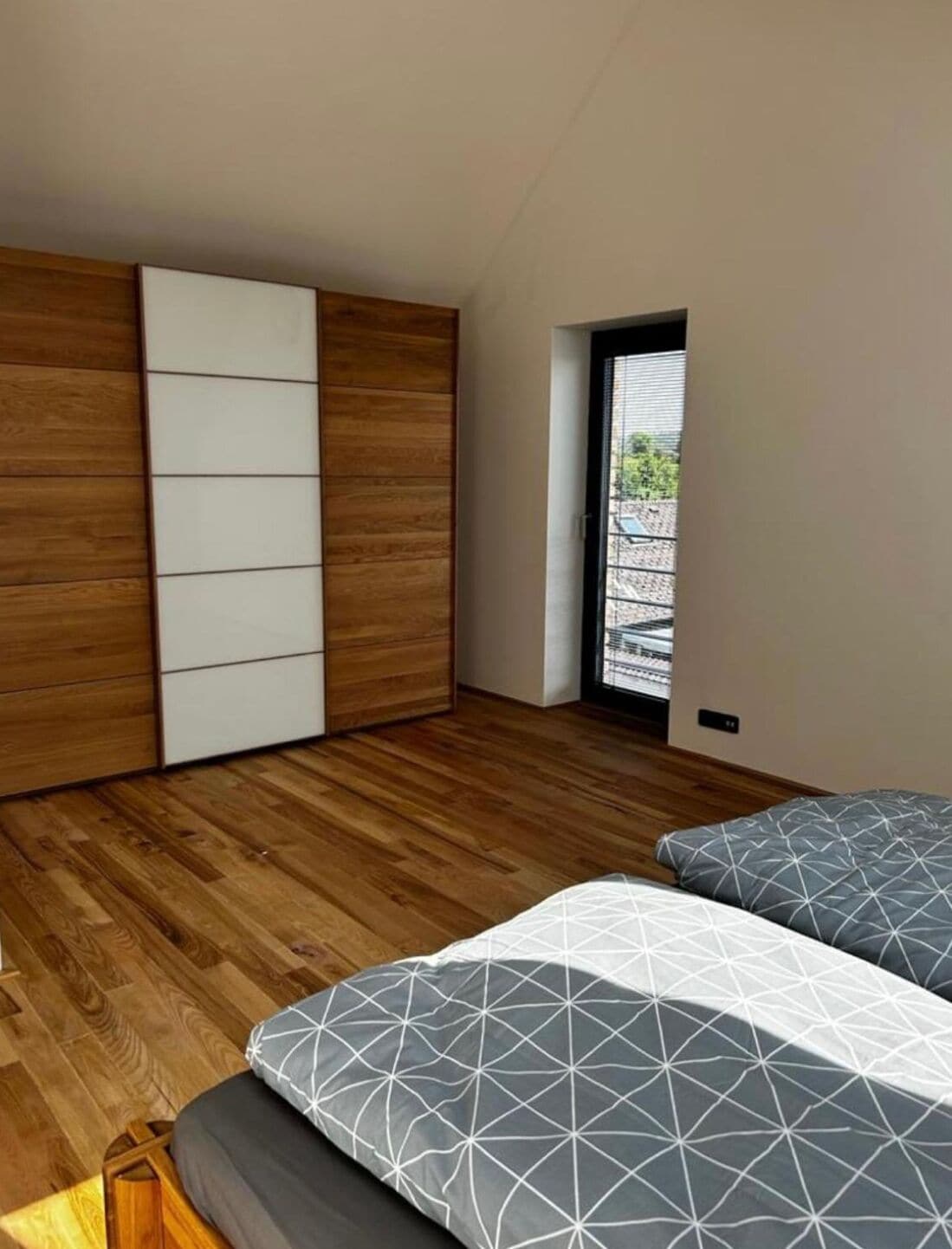 Une chambre avec un plancher en bois, un lit avec une literie à motifs, une armoire à portes coulissantes et une vue sur l’extérieur, visible à travers une porte.