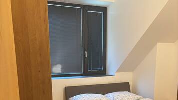 Een slaapkamer met een houten bed, een raam met zonwering en een schuine kap.