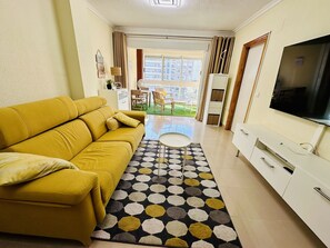A living room with a yellow sofa, a TV, and a patterned rug.