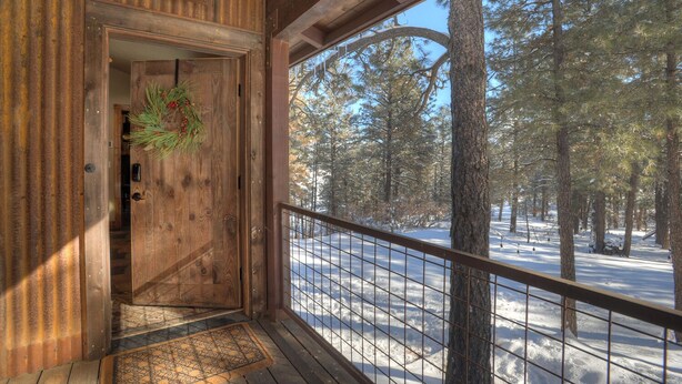 Eine Holzhütte mit einer Tür, die auf eine mit Schnee bedeckte Terrasse führt.