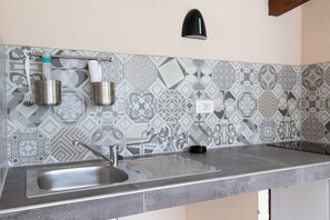 A kitchen with a stainless steel sink, a black wall-mounted light, and patterned backsplash tiles. - Villa Casa Kalandra Zadarvillas (Rovinj)