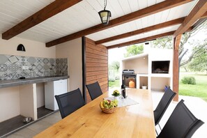 Un espacio exterior para comer con una mesa de madera, sillas negras, una cesta de fruta y un farol colgante.