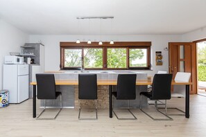 Una cocina moderna con una isla central, sillas negras, horno empotrado y un ventanal amplio.
