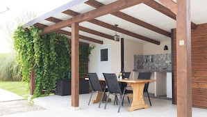 Eine Terrasse im Freien mit einem Holztisch und -stühlen, einer Küchenzeile mit Fliesenrückwand und einer Pergola aus Holz.