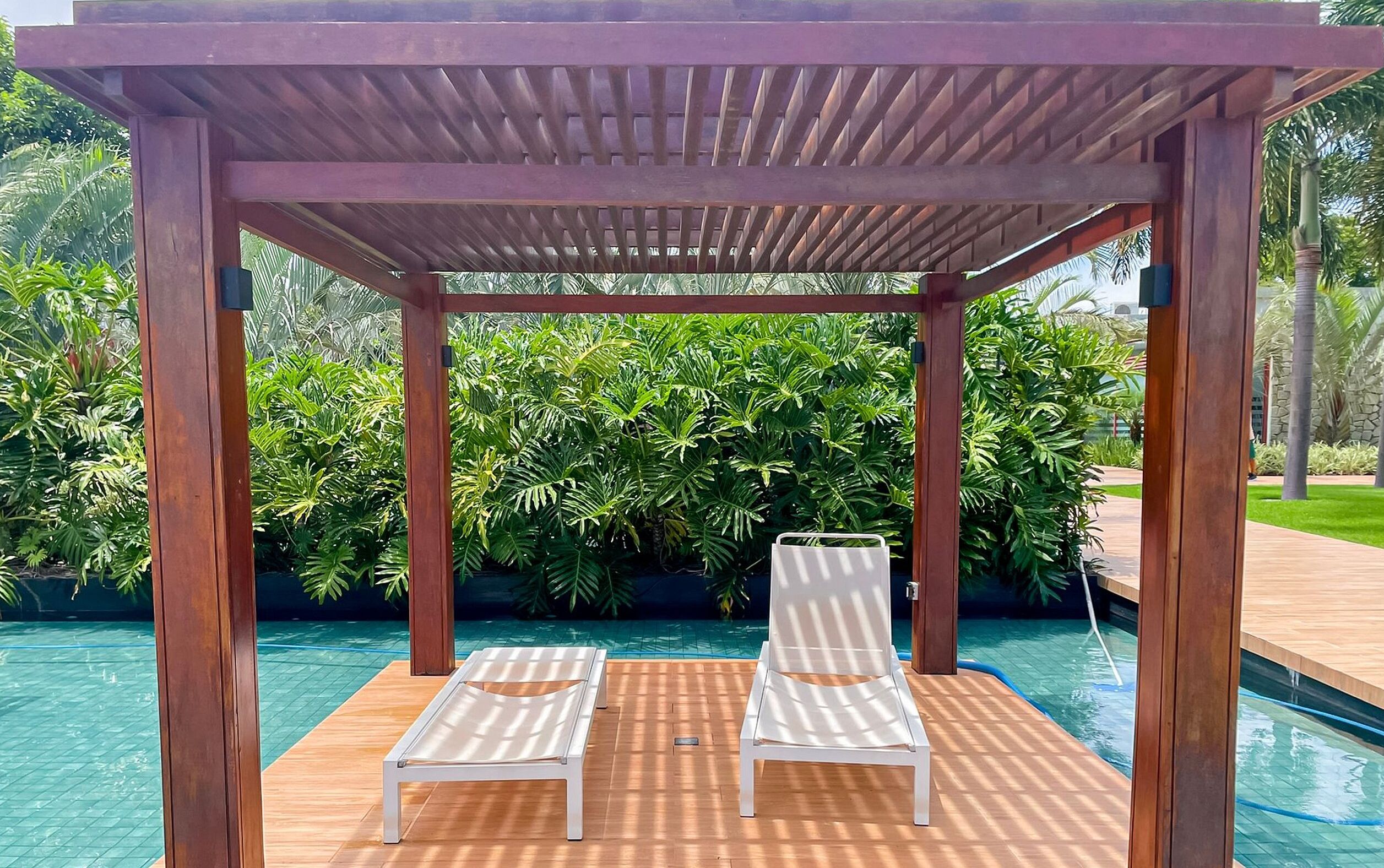 Una pérgola de madera con dos sillones blancos junto a una piscina.