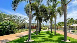 A well-maintained garden with palm trees, a pool area, and a pathway. - Flat Ilê de Pipa Oásis - By Almare (Tibau do Sul)