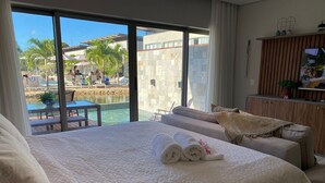 A hotel room with a large bed, a wooden cabinet, and a view of a pool area. - Flat Ilê de Pipa Oásis - By Almare (Tibau do Sul)