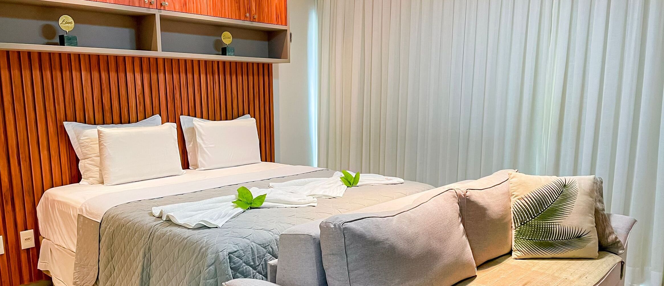 A modern hotel room with a large bed, a sofa, and a wooden accent wall.