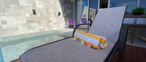 A poolside lounge chair with a towel and plush toy, a stone wall, and a glass door leading to a patio area.