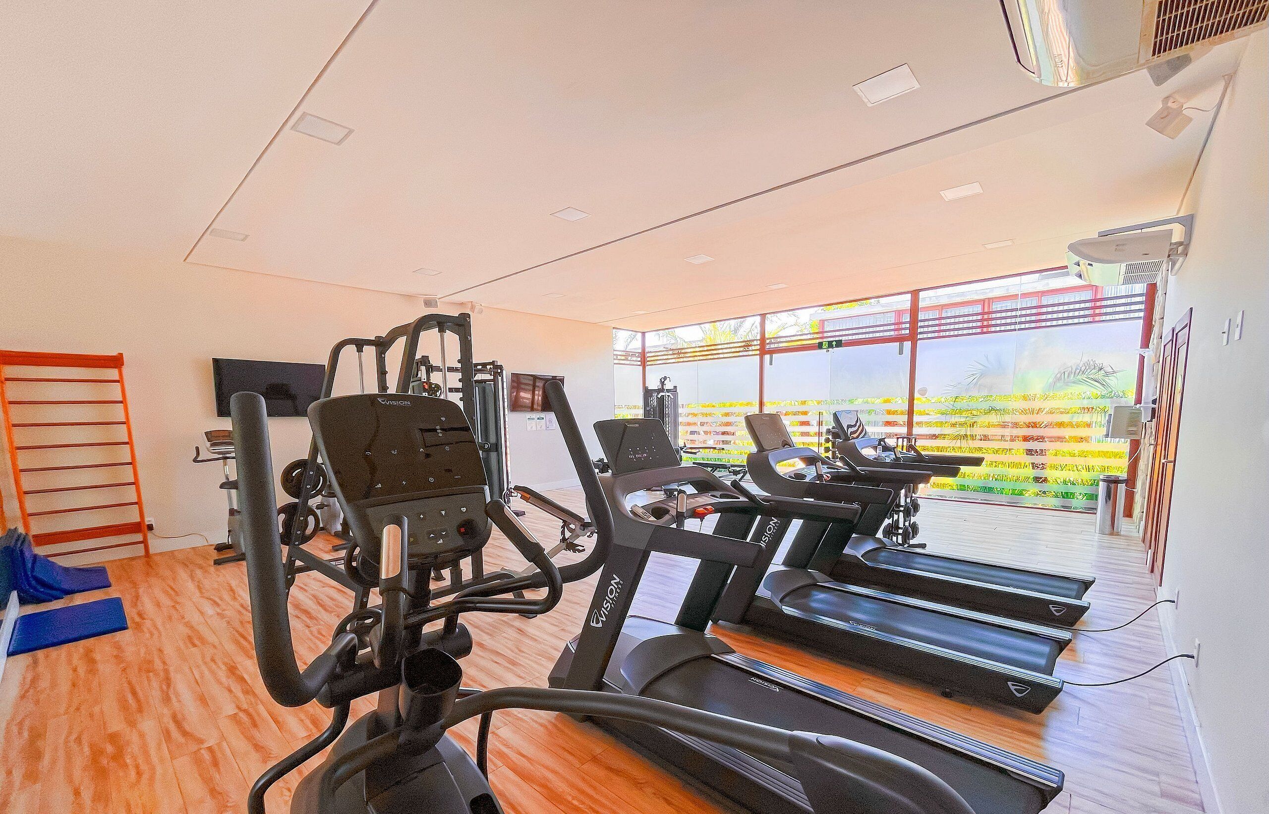 Un gimnasio con equipo de ejercicio, una cinta de correr y vistas a un edificio de techo rojo.