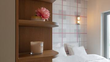 Een slaapkamer met een bed, een nachtkastje met boeken en een kaars, een wandlamp en een raam.