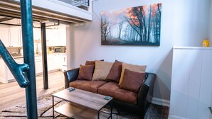A modern living room with a sofa, coffee table, and a painting of a forest. - Lafayette Vibe Downtown District (Lafayette)