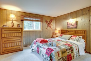 A bedroom with a wooden paneled wall, a bed with a quilt, a window with blinds, and a wall-mounted cross. - Country Vacation Rental in Mercer at Waterfall! (Mercer)