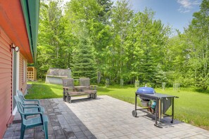 A patio with outdoor furniture, a barbecue grill, and a shed in a wooded area.