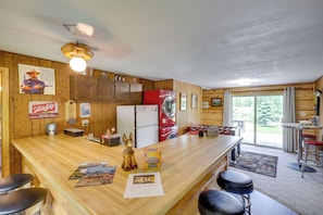 A wooden cabin interior with a kitchen area, bar stools, a washing machine, and a large window. - Country Vacation Rental in Mercer at Waterfall! (Mercer)