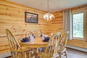 A wooden-paneled room with a round wooden table, six chairs, a hanging light fixture, a framed picture on the wall, and a window with curtains. - Country Vacation Rental in Mercer at Waterfall! (Mercer)
