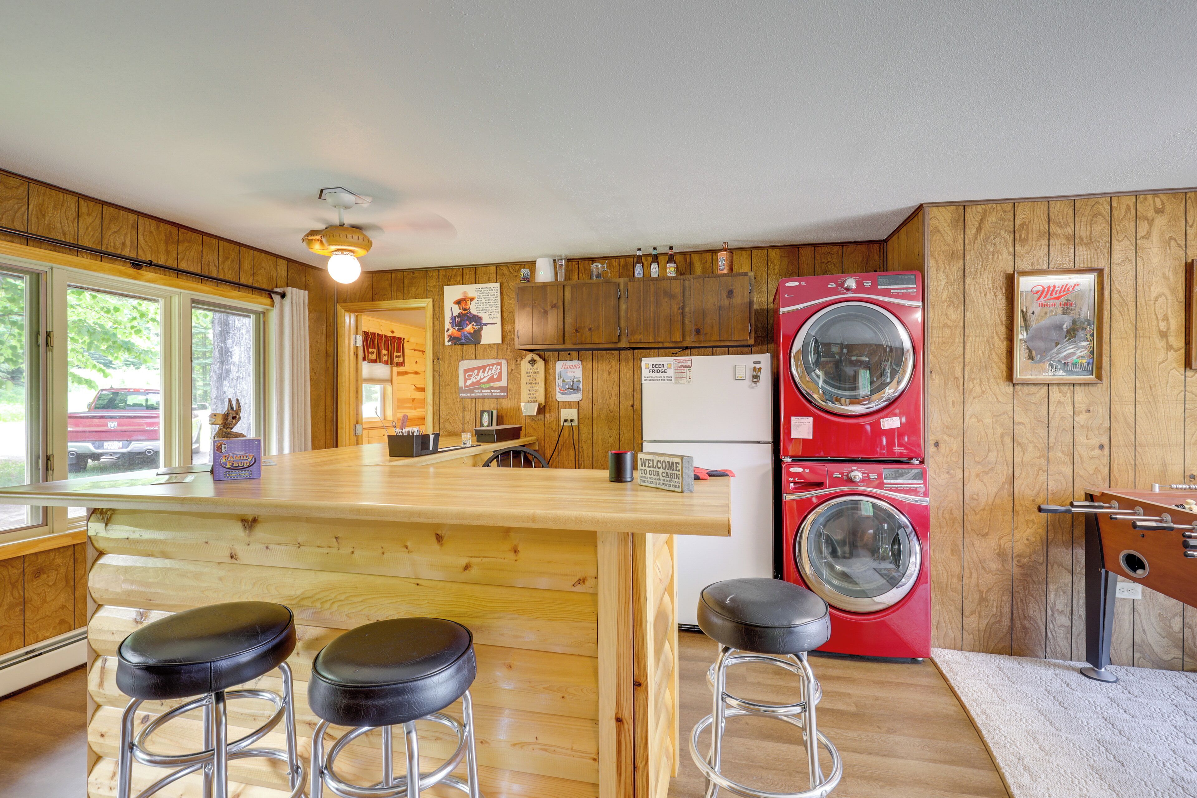 Une cuisine avec des meubles en bois, un lave-linge rouge et un coin bar avec des tabourets.