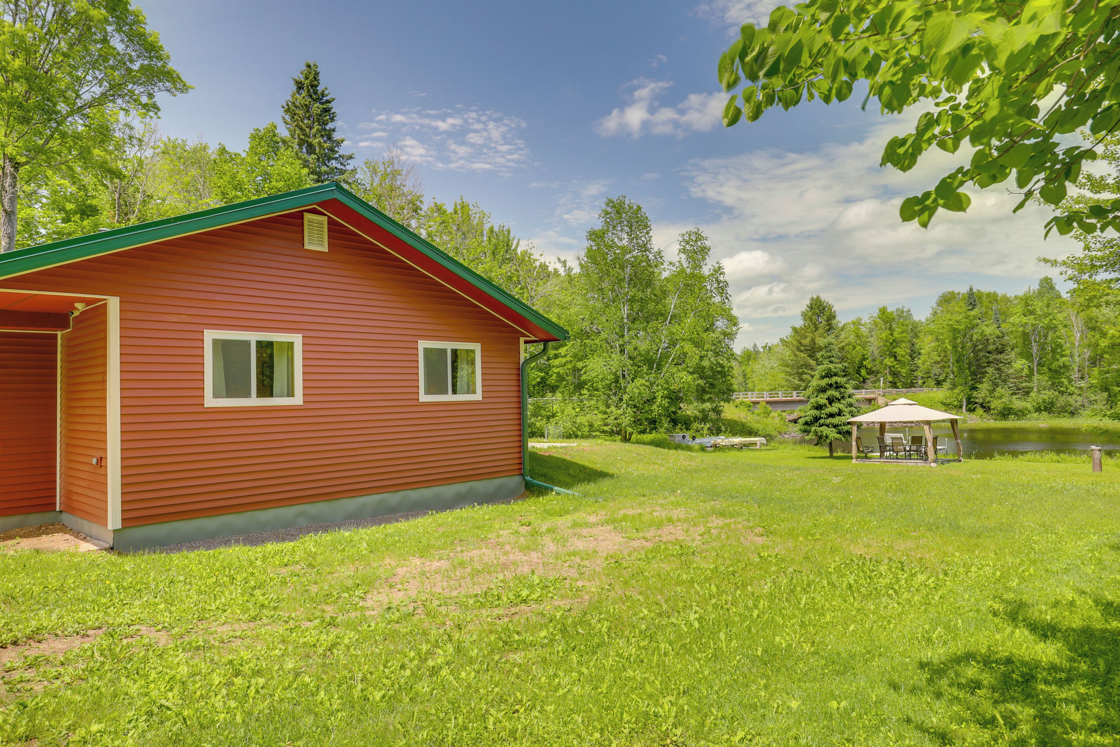 A wooden cabin with a green roof, a small deck, and a pond in the background.