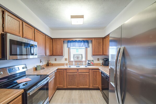 A kitchen with wooden cabinets, stainless steel appliances, a window with blue valance, and a built-in oven. - Welcoming Condo in Davenport: Central Location! (Davenport)