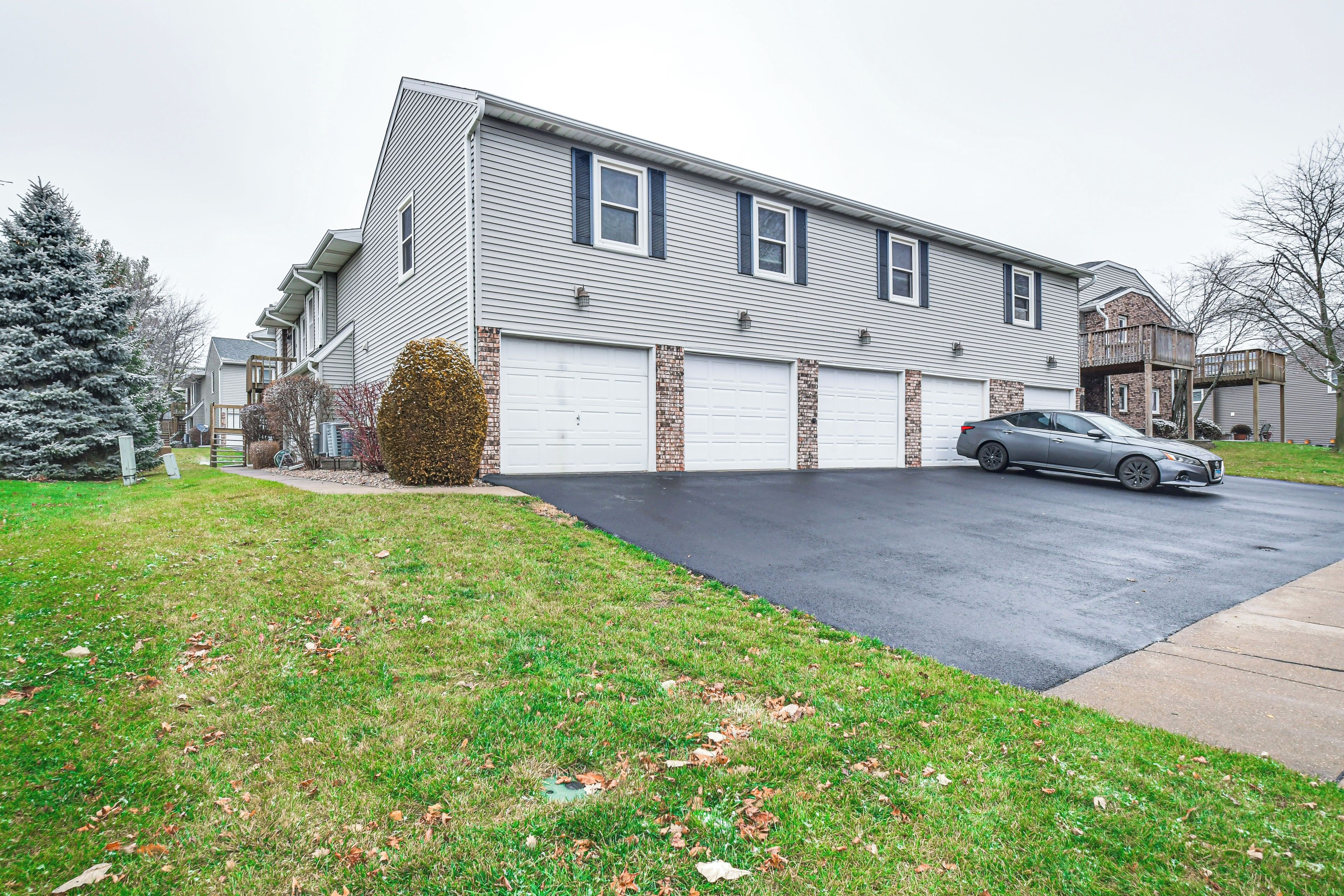 A two-story residential building with a garage, a driveway, and a parked car.
