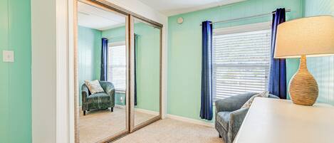 A room with teal walls, a ceiling fan, a large mirror, a sofa, a lamp, and a window with blinds.