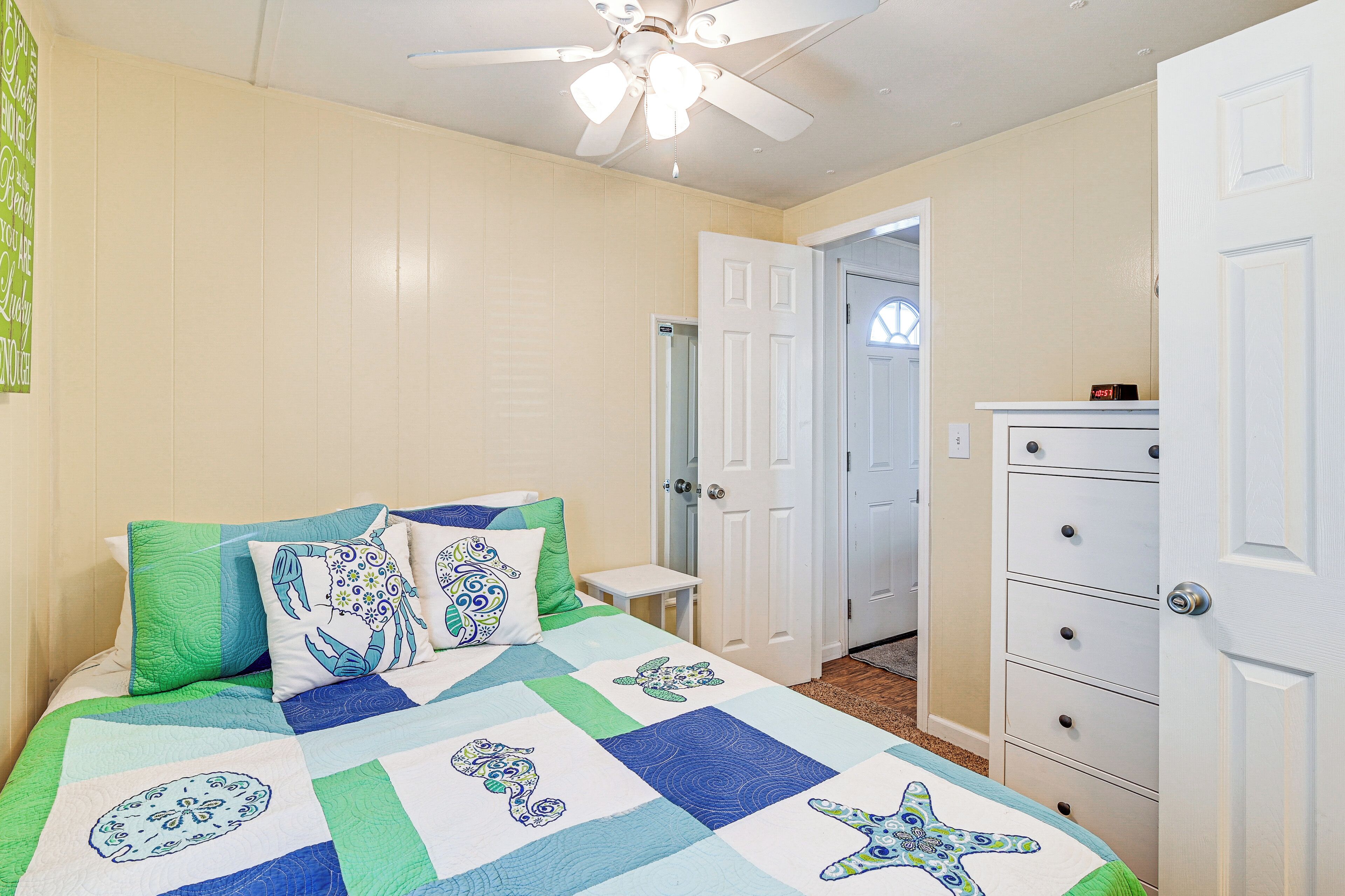 Un dormitorio con cama, ventilador de techo, cómoda y puerta que da a otra habitación.