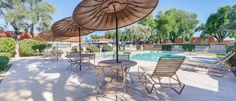 A poolside area with lounge chairs, a table, and two large umbrellas.