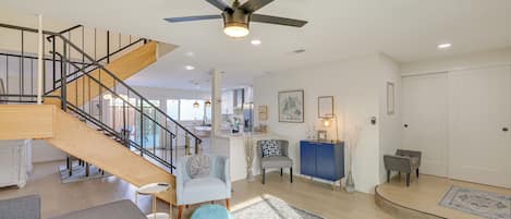 A spacious living area with a staircase, a ceiling fan, and a kitchen in the background.