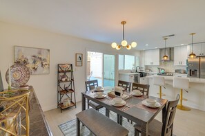 Une cuisine moderne avec des meubles blancs, un coin repas doté d’une table en bois pour quatre personnes et une grande fenêtre laissant entrer la lumière naturelle.