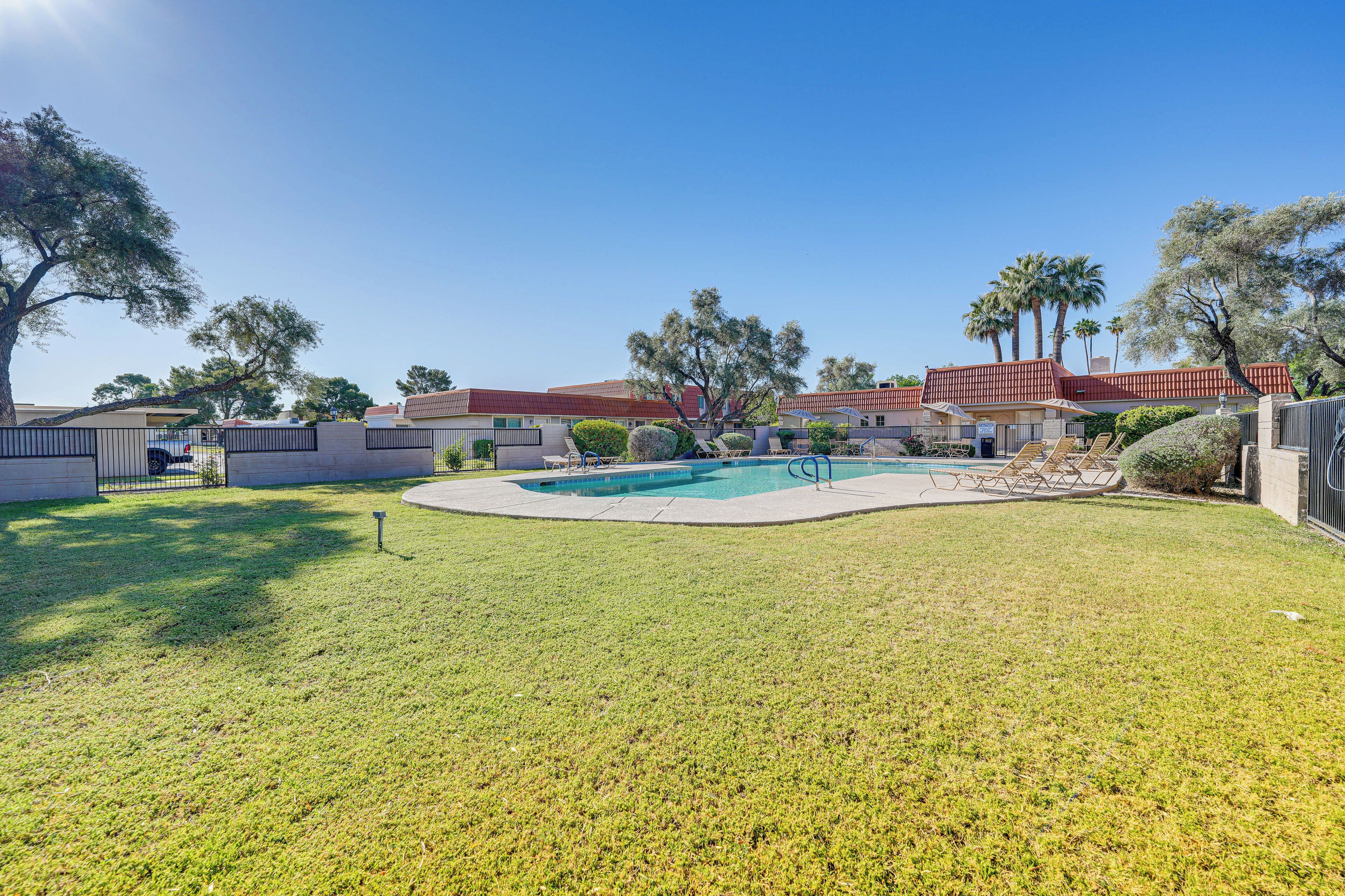 A backyard with a swimming pool, a covered patio, and a fenced area with trees.