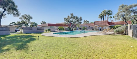 A backyard with a swimming pool, a covered patio, and a fenced area with trees.